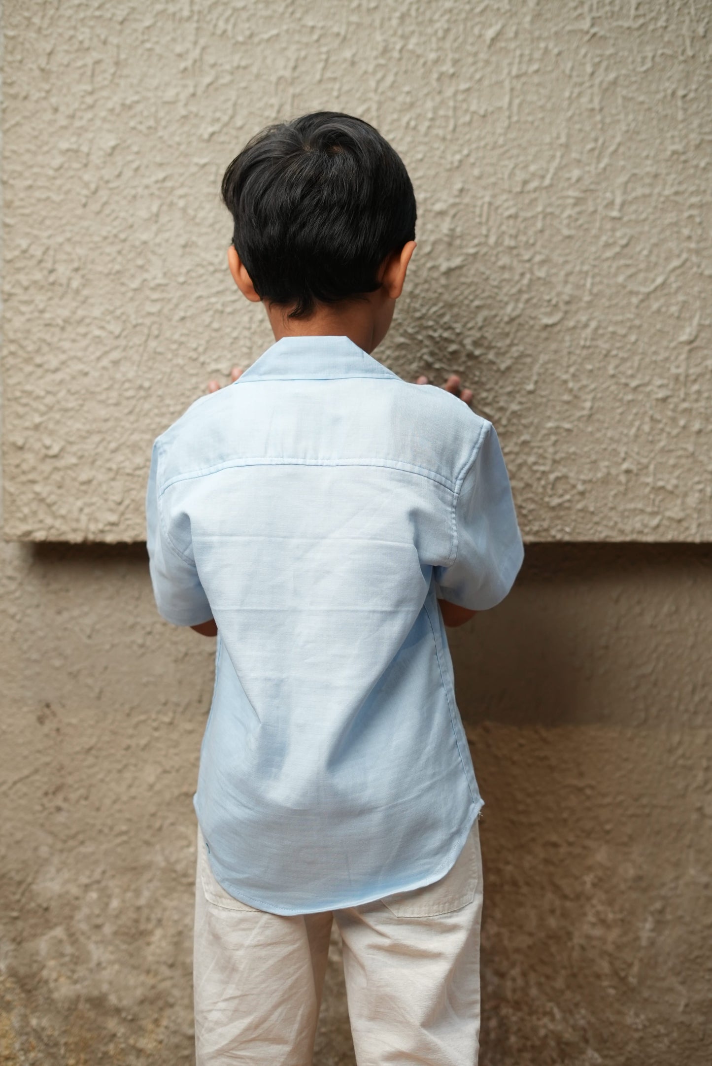 Person wearing a light blue shirt and beige pants standing on a carpeted floor.