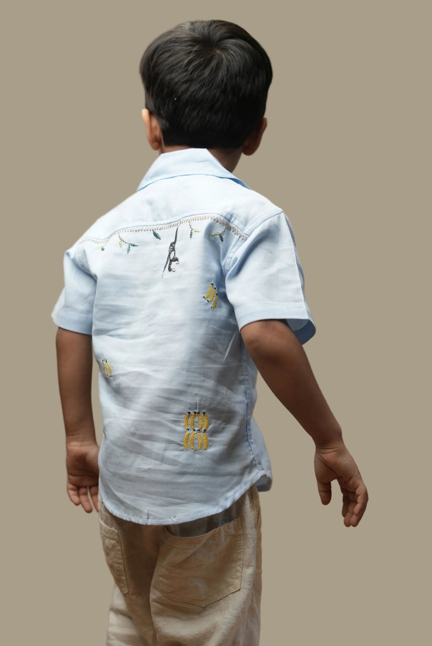Child wearing a light blue denim shirt with embroidered designs on a plain background