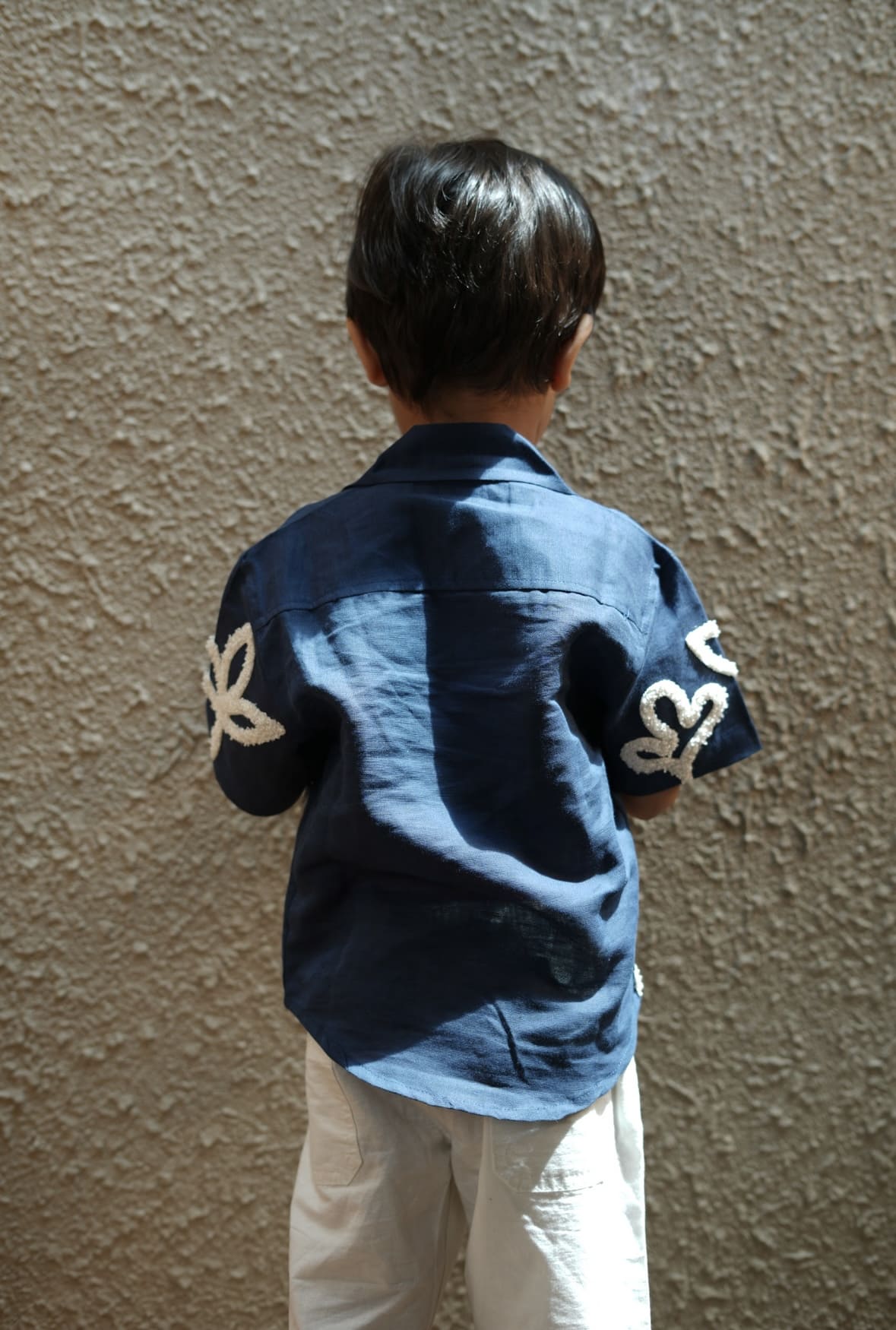 Child wearing a blue shirt with white patterns against a beige wall