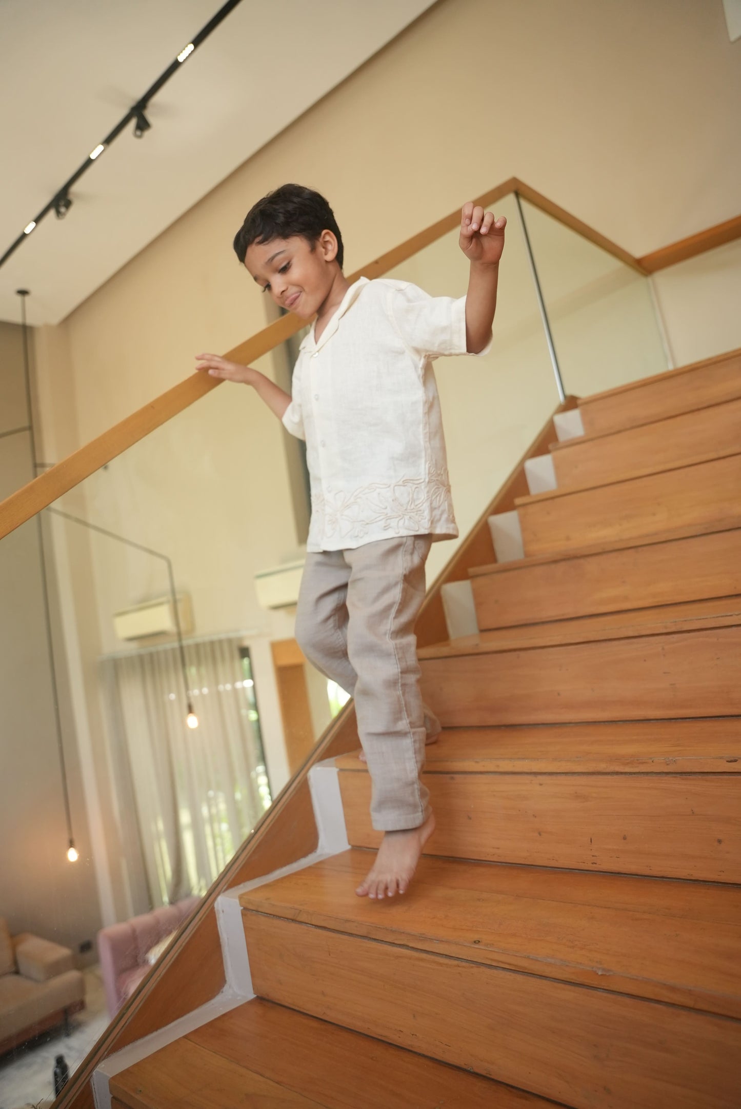 Child standing on a wooden staircase with a glass balustrade