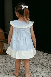 Child wearing a light blue dress with white ruffled details, standing on a textured surface.