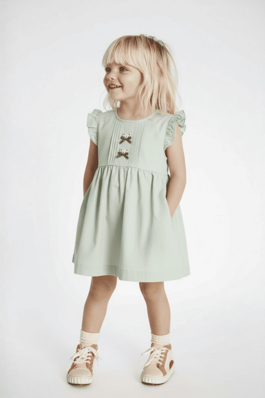 Young girl wearing a light green dress with lace details on a white background