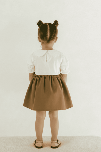 Child wearing a white shirt and brown skirt on a plain background