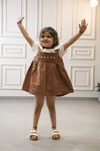 Young girl in a brown dress with white lace collar standing in a room with white paneled walls.