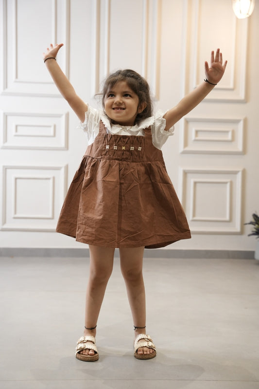 Young girl in a brown dress with white lace collar standing in a room with white paneled walls.
