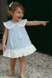 Young girl in a light blue dress with white ruffled collar and skirt, pointing forward.
