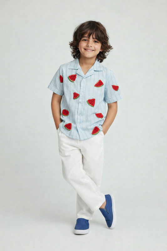 Child wearing a light blue shirt with red fruit patterns and white pants on a plain background