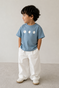 Child wearing a blue t-shirt with white circle designs and white pants on a plain background