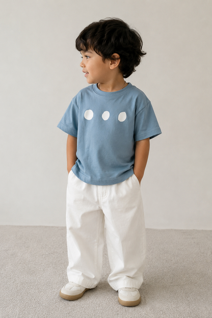 Child wearing a blue t-shirt with white circle designs and white pants on a plain background