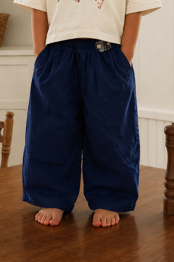 Child standing on a wooden floor wearing a white t-shirt with graphics and dark blue pants.