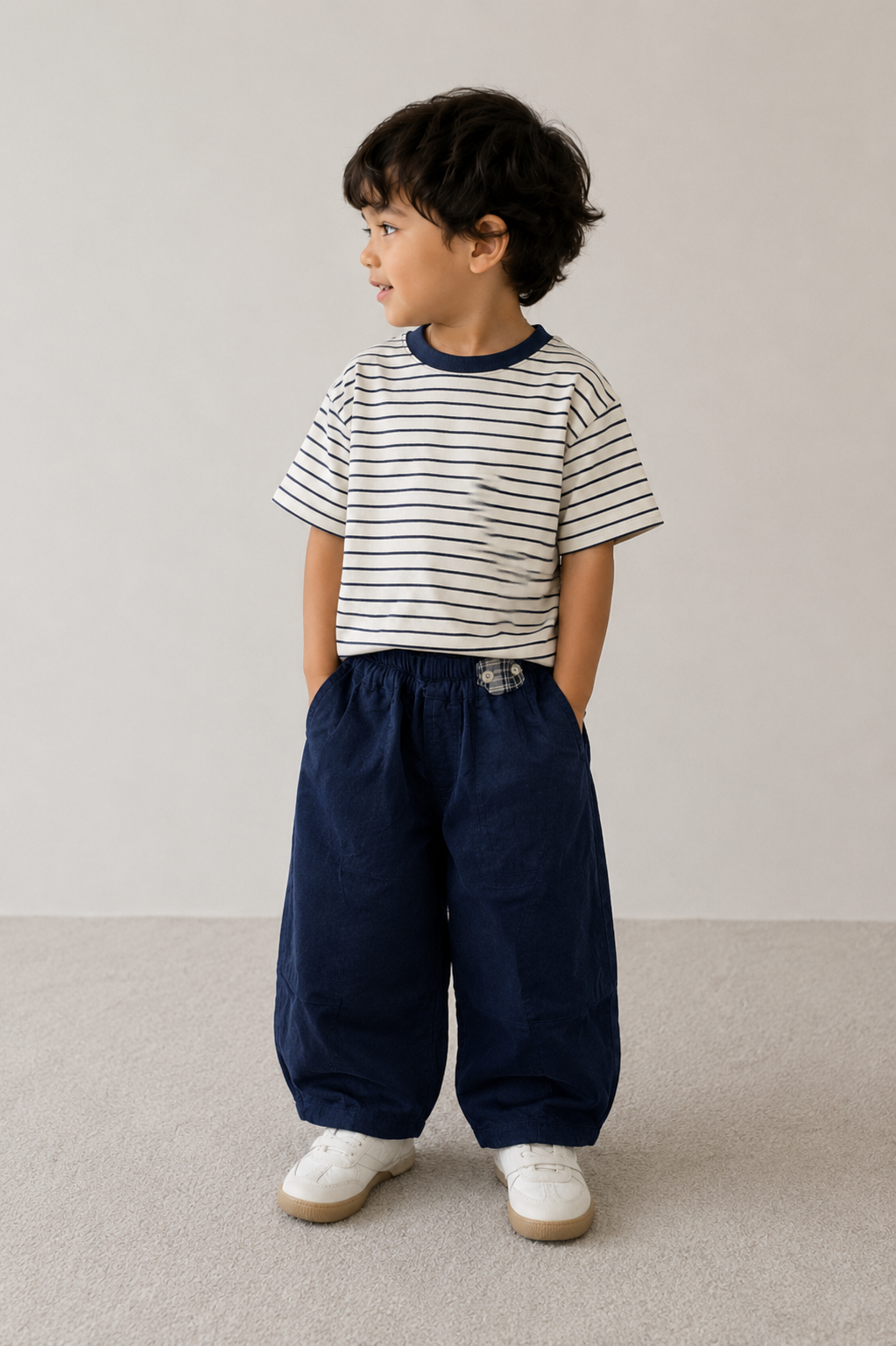 Child wearing a striped shirt and navy pants standing on a plain background