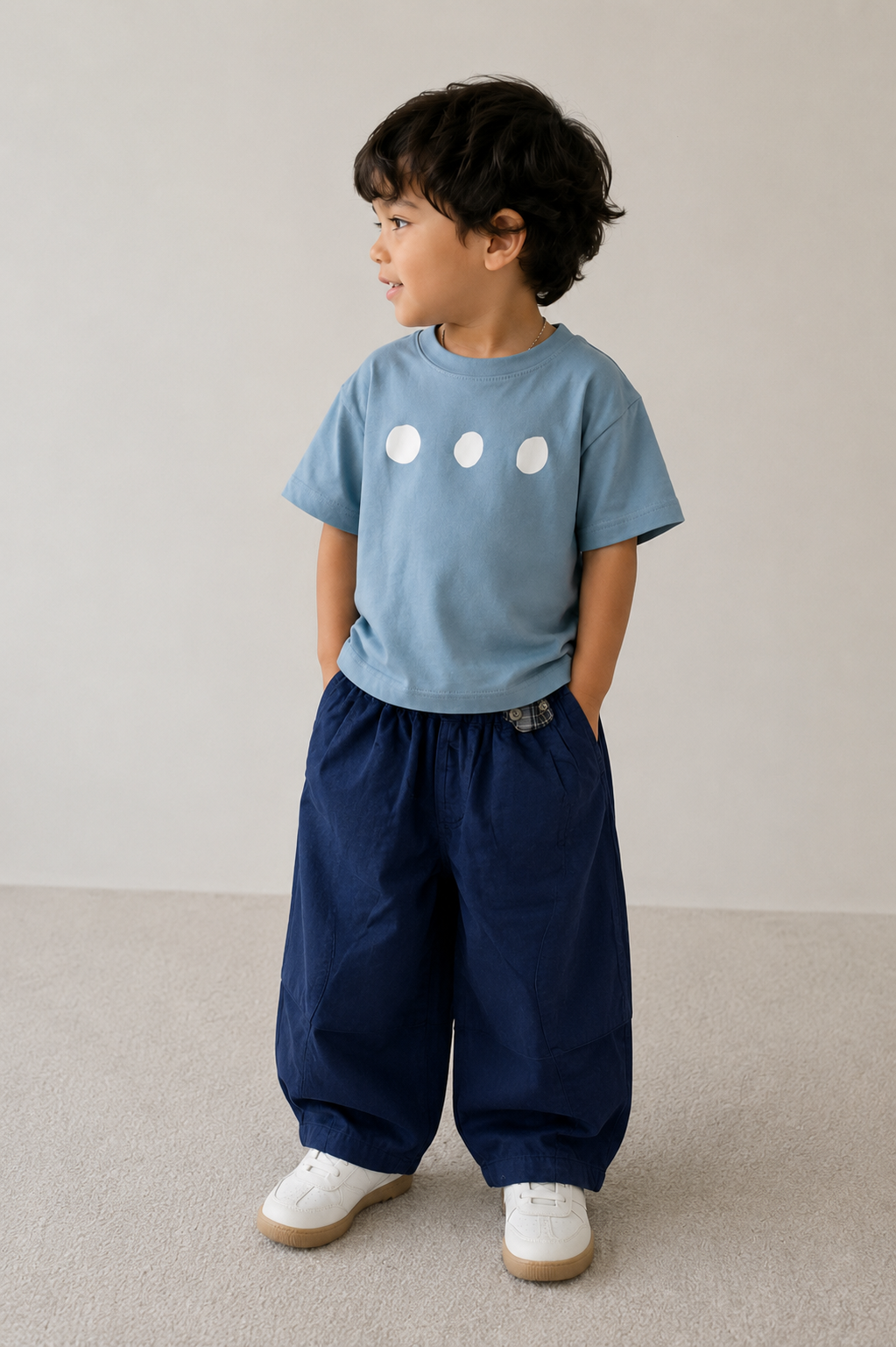 Child wearing a blue t-shirt and navy pants standing on a neutral background