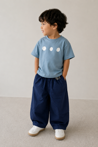 Child wearing a blue t-shirt and navy pants standing on a neutral background