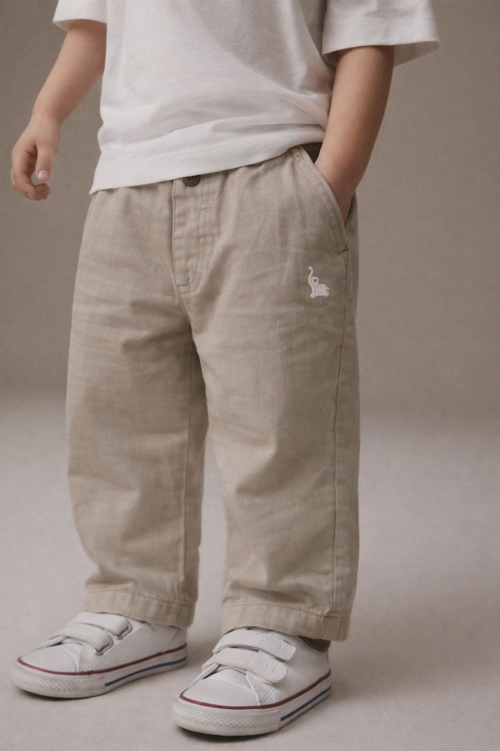 Person wearing beige pants with a small logo and white sneakers on a neutral background