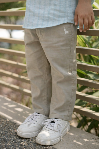 Person wearing beige pants and white sneakers standing on a wooden deck with greenery in the background