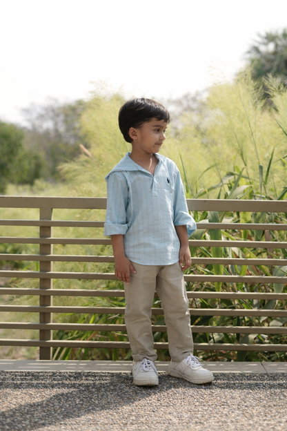 Child standing outdoors near a wooden railing with greenery in the background