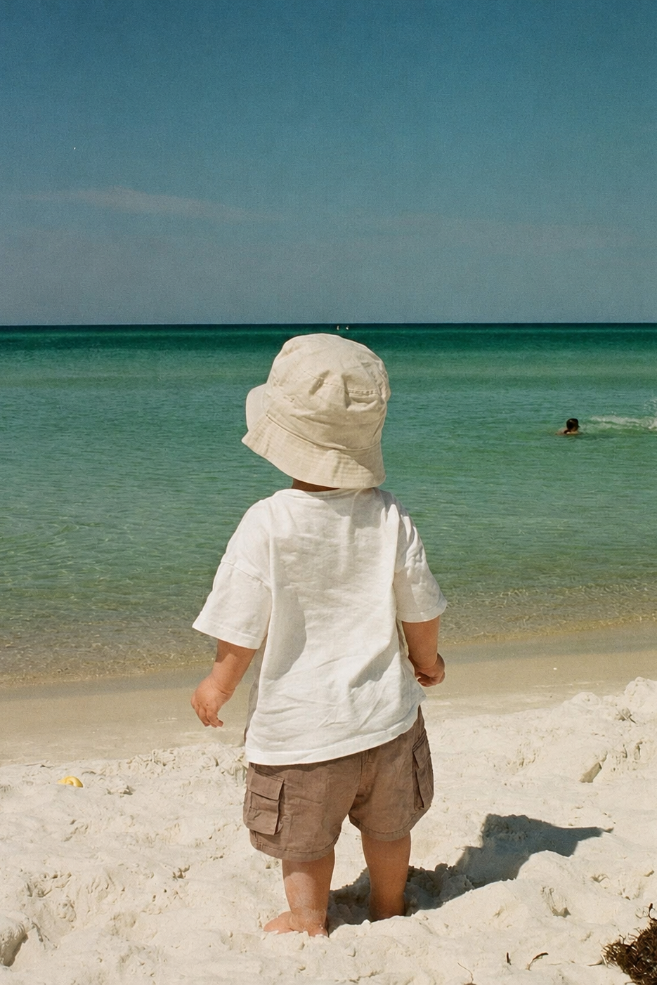 Child wearing a hat on a beach looking at the ocean