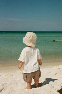 Child wearing a hat on a beach looking at the ocean