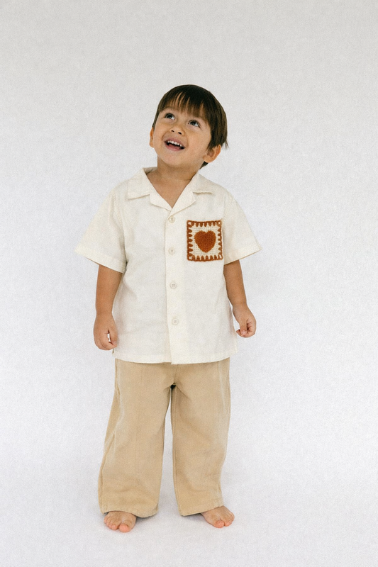 Child wearing a white shirt with a heart design and beige pants on a white background