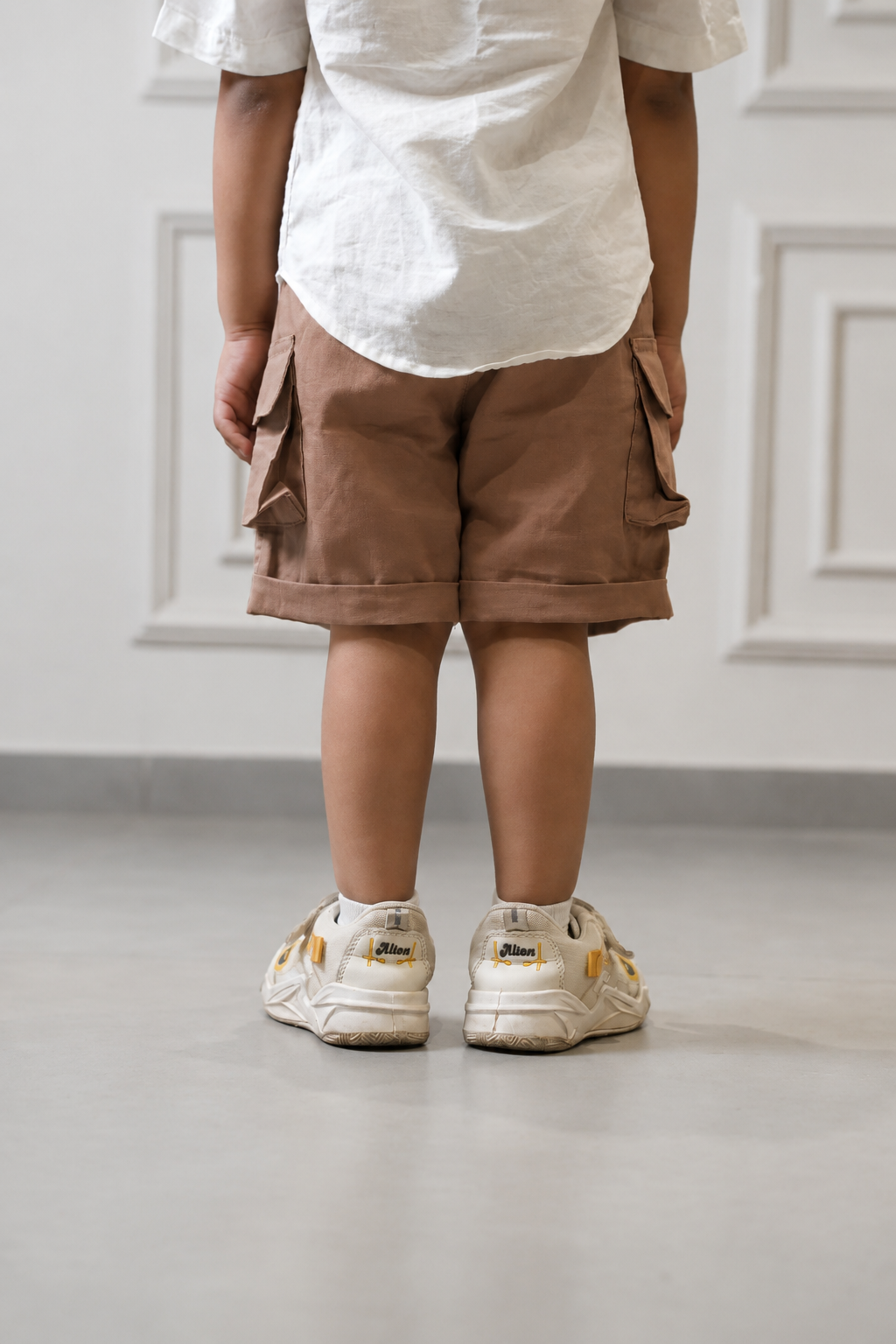 Person wearing a white shirt, brown shorts, and white sneakers on a light gray floor.