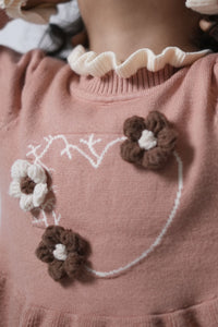 Close-up of a pink sweater with floral decorations and a heart design.