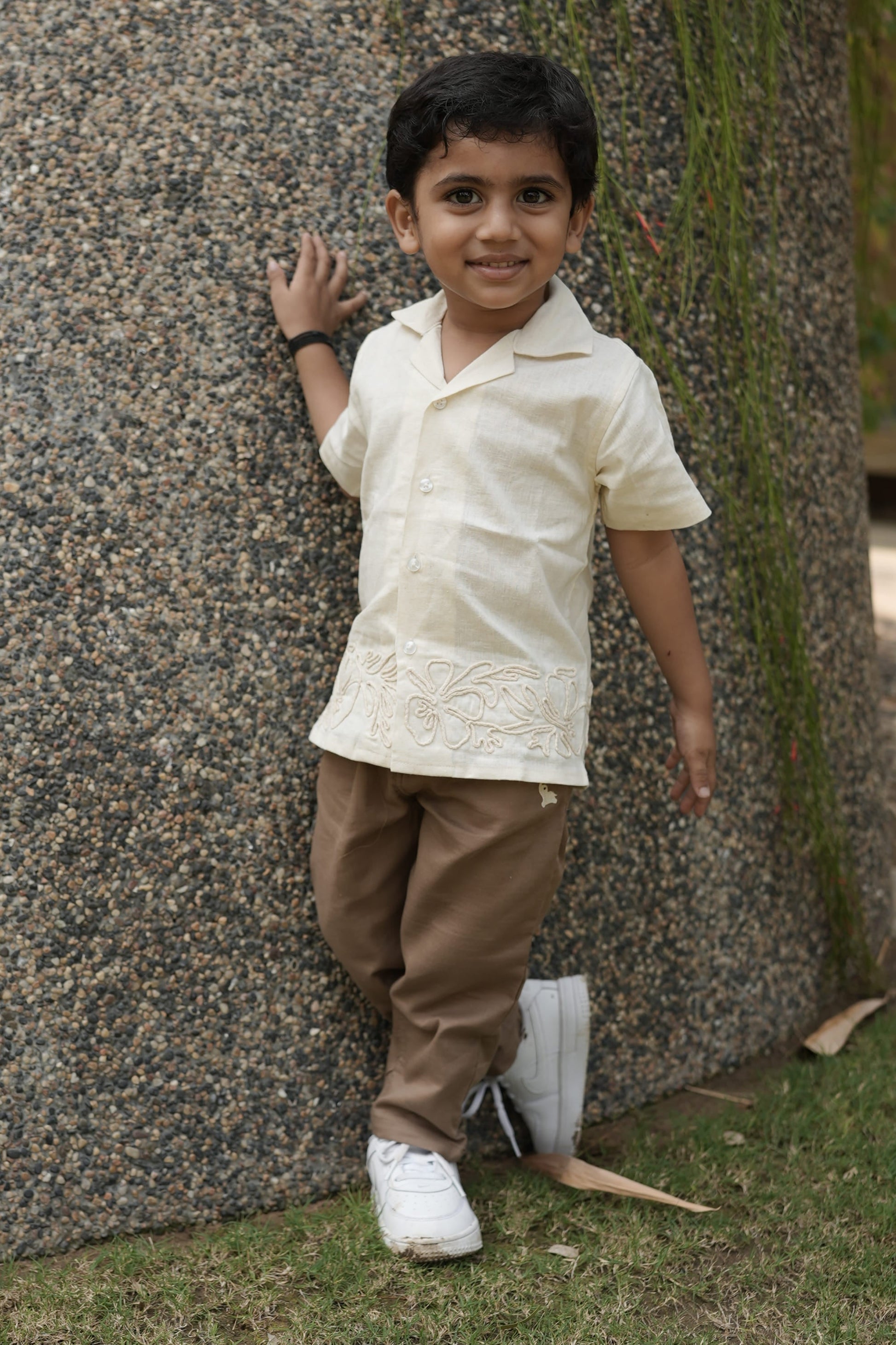 Child lying on a large stone with grass and a tree in the background