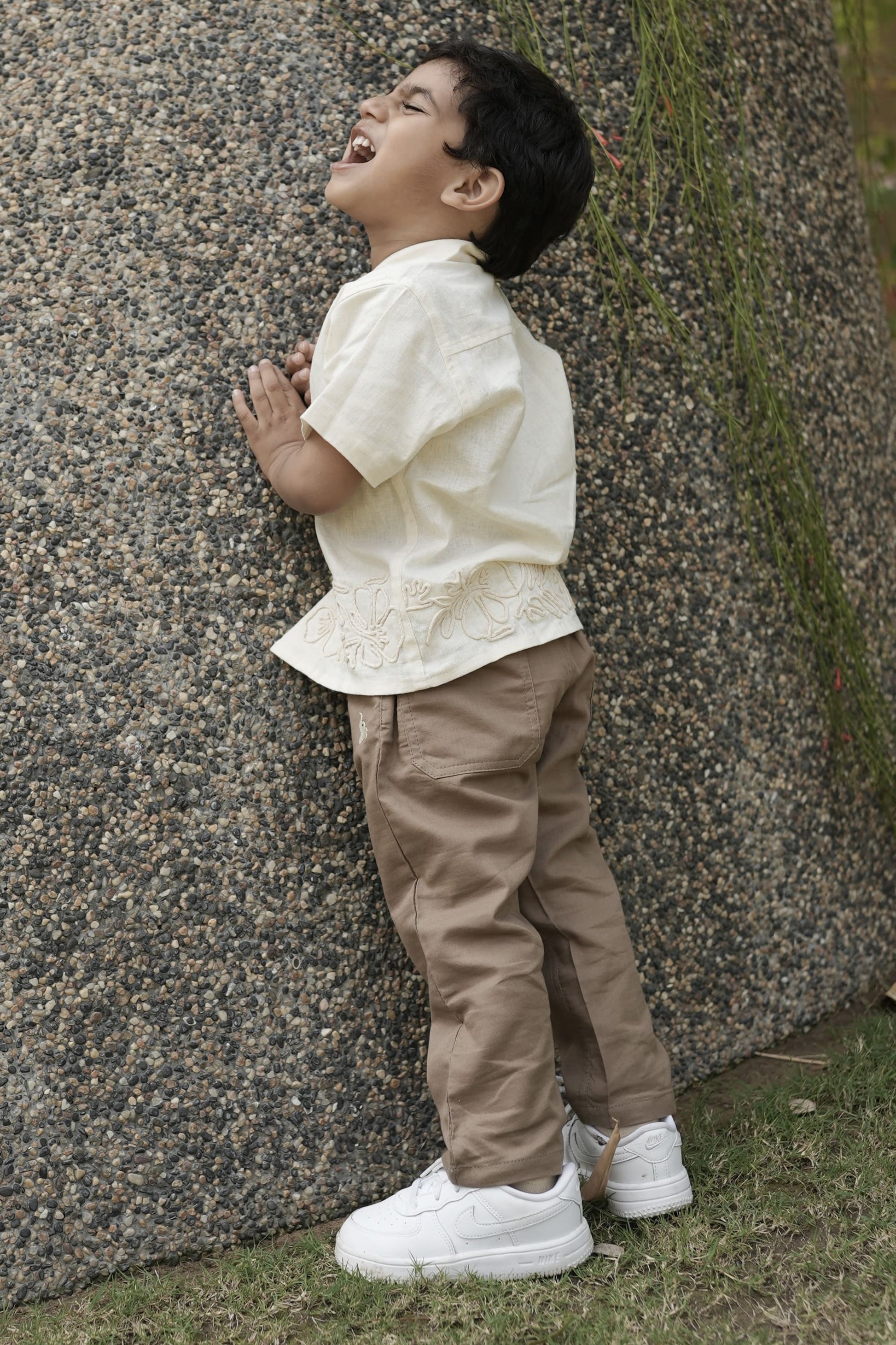 Child standing next to a large tree trunk in an outdoor setting