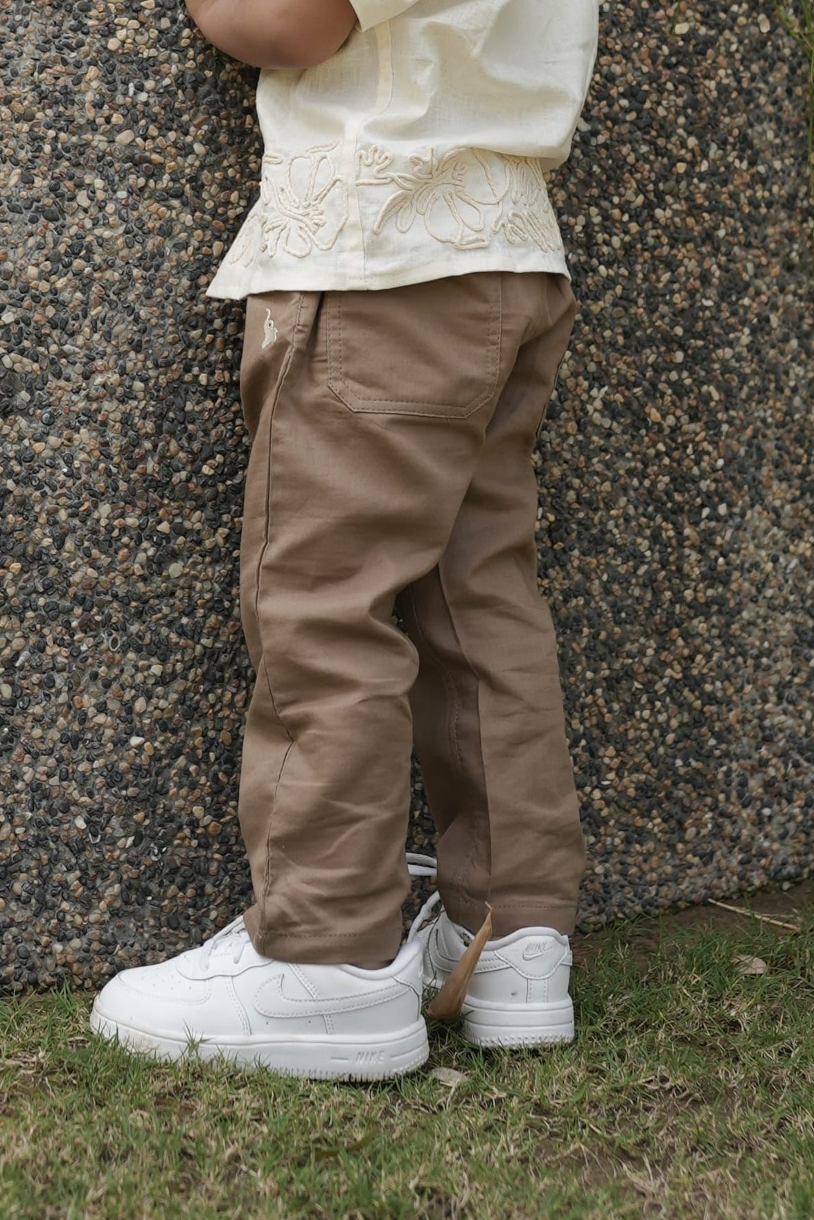 Child standing on a gravel path with grass and trees in the background