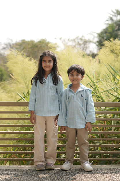 Two kids standing outdoors with a wooden fence and greenery in the background