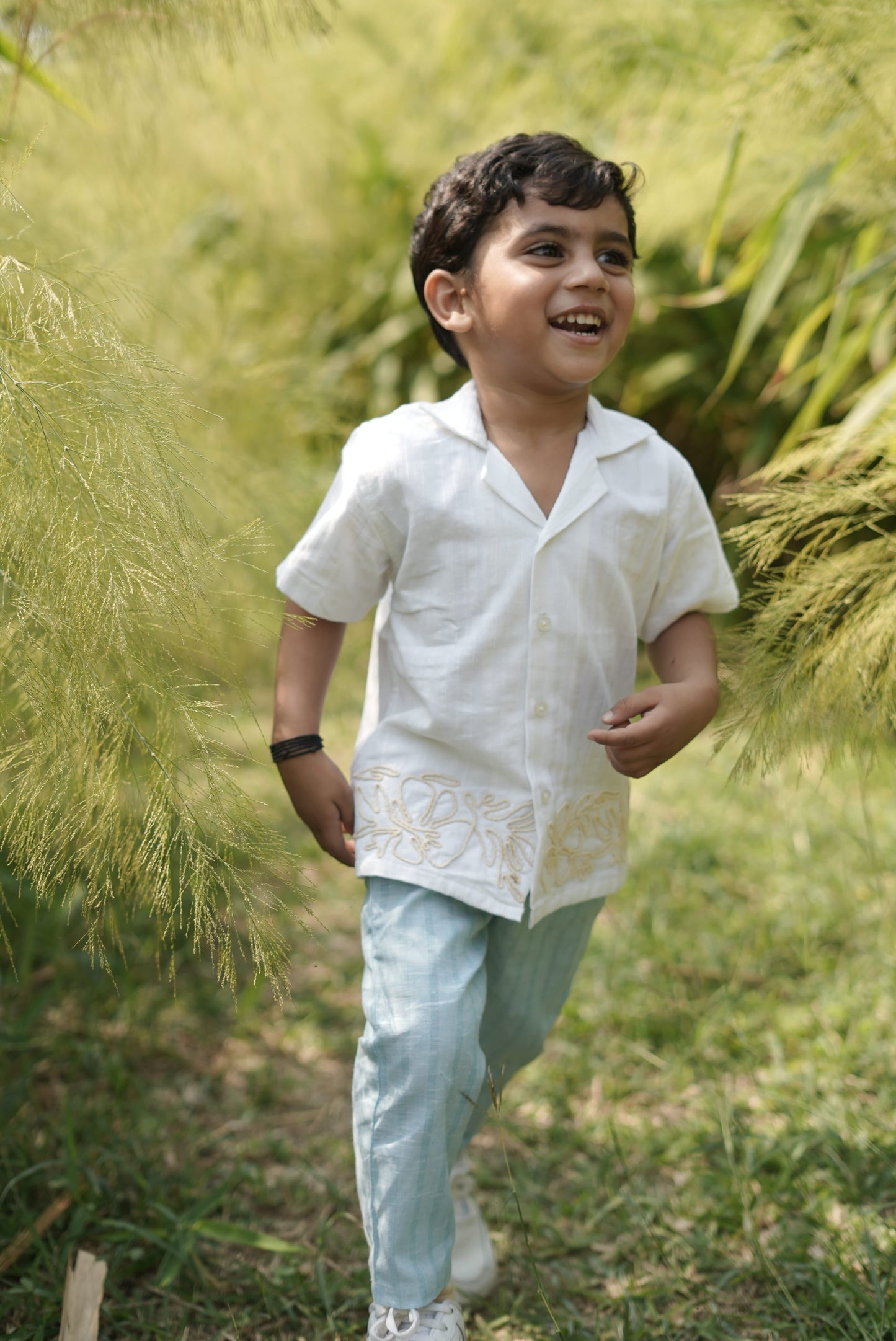 Child in a white shirt and light blue pants standing in tall grass