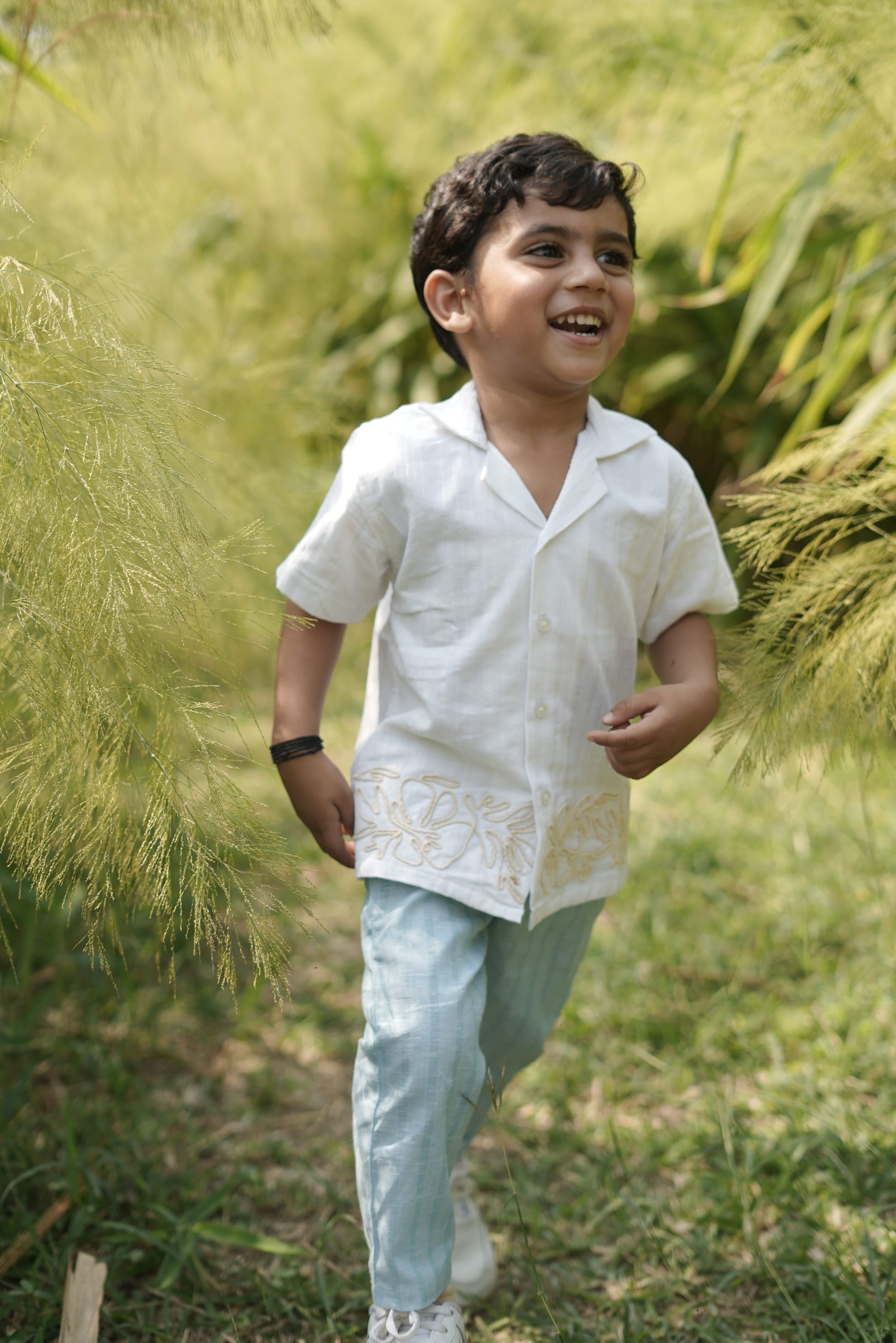 Child in a white shirt and light blue pants standing in tall grass