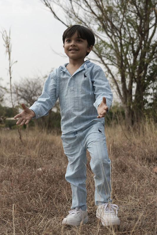 Child in a light blue outfit standing in a field with trees in the background