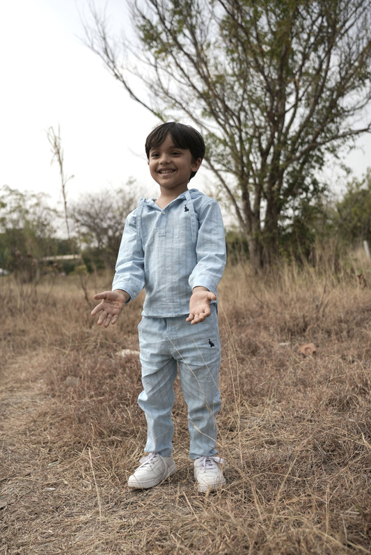 Child wearing a light blue outfit standing in a field with trees in the background