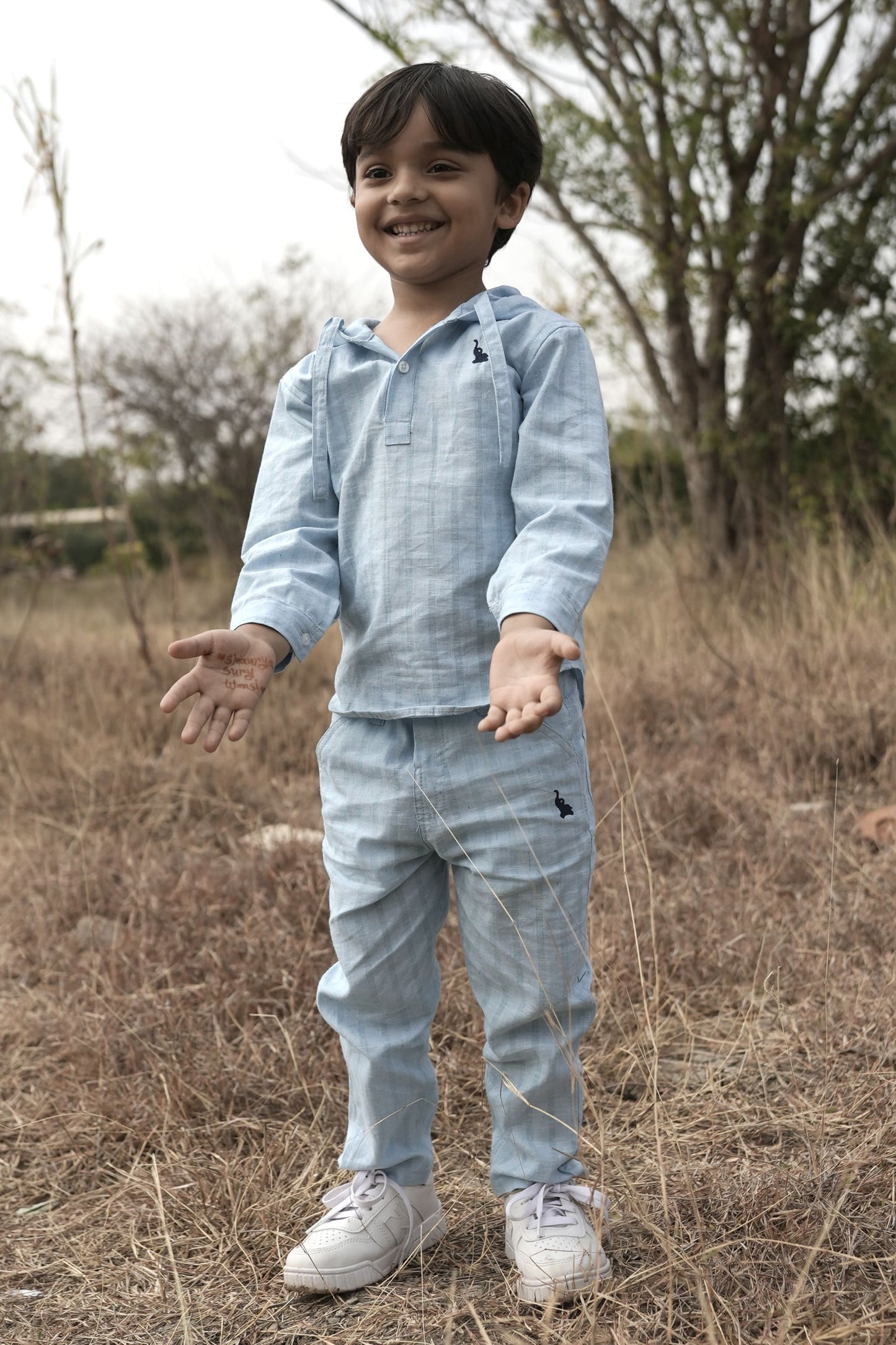 Child wearing a light blue outfit standing in a field with trees in the background