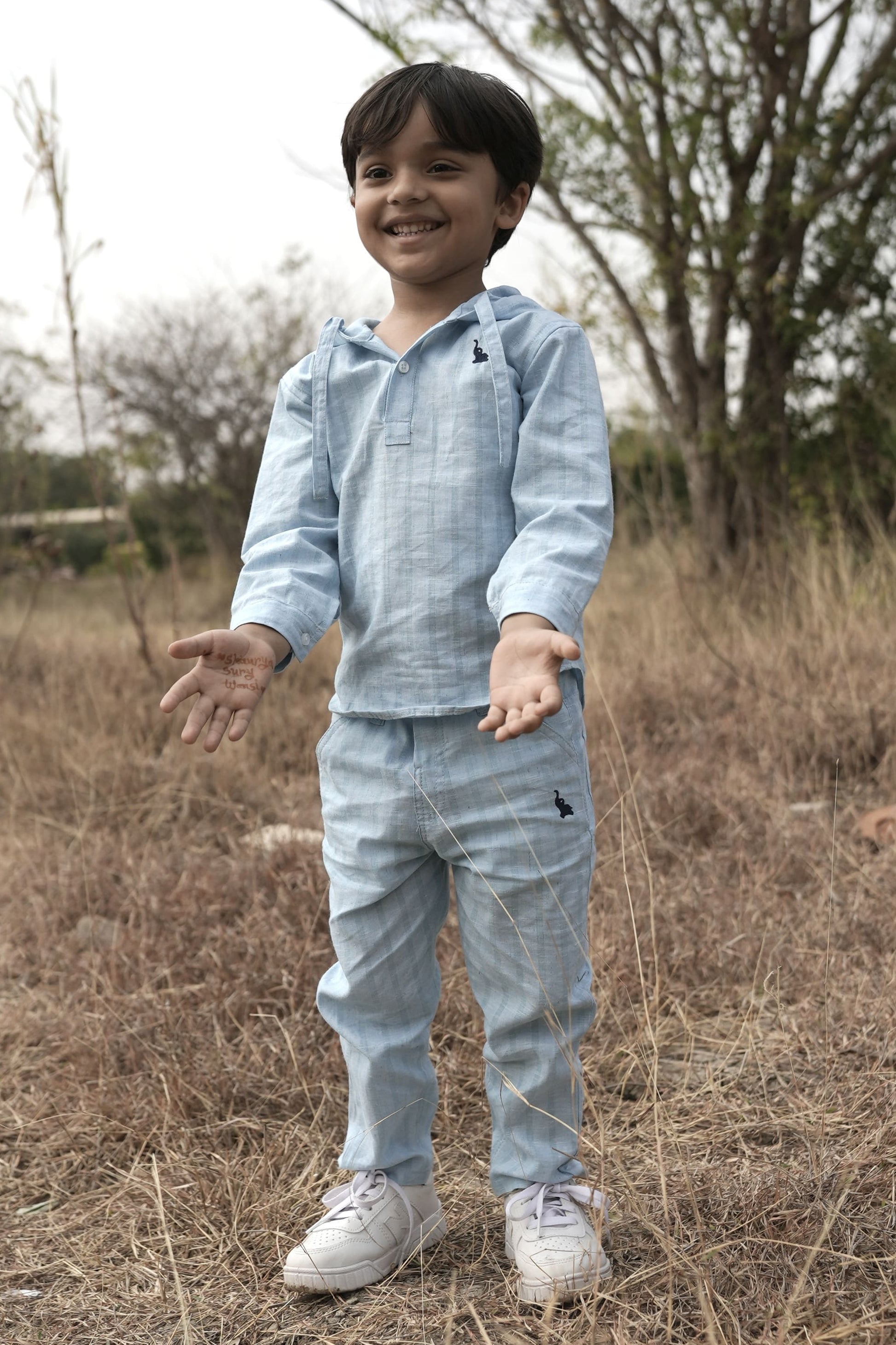 Child wearing a light blue outfit standing in a field with trees in the background
