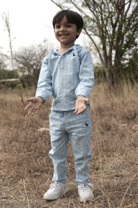 Child wearing a light blue outfit standing in a field with trees in the background