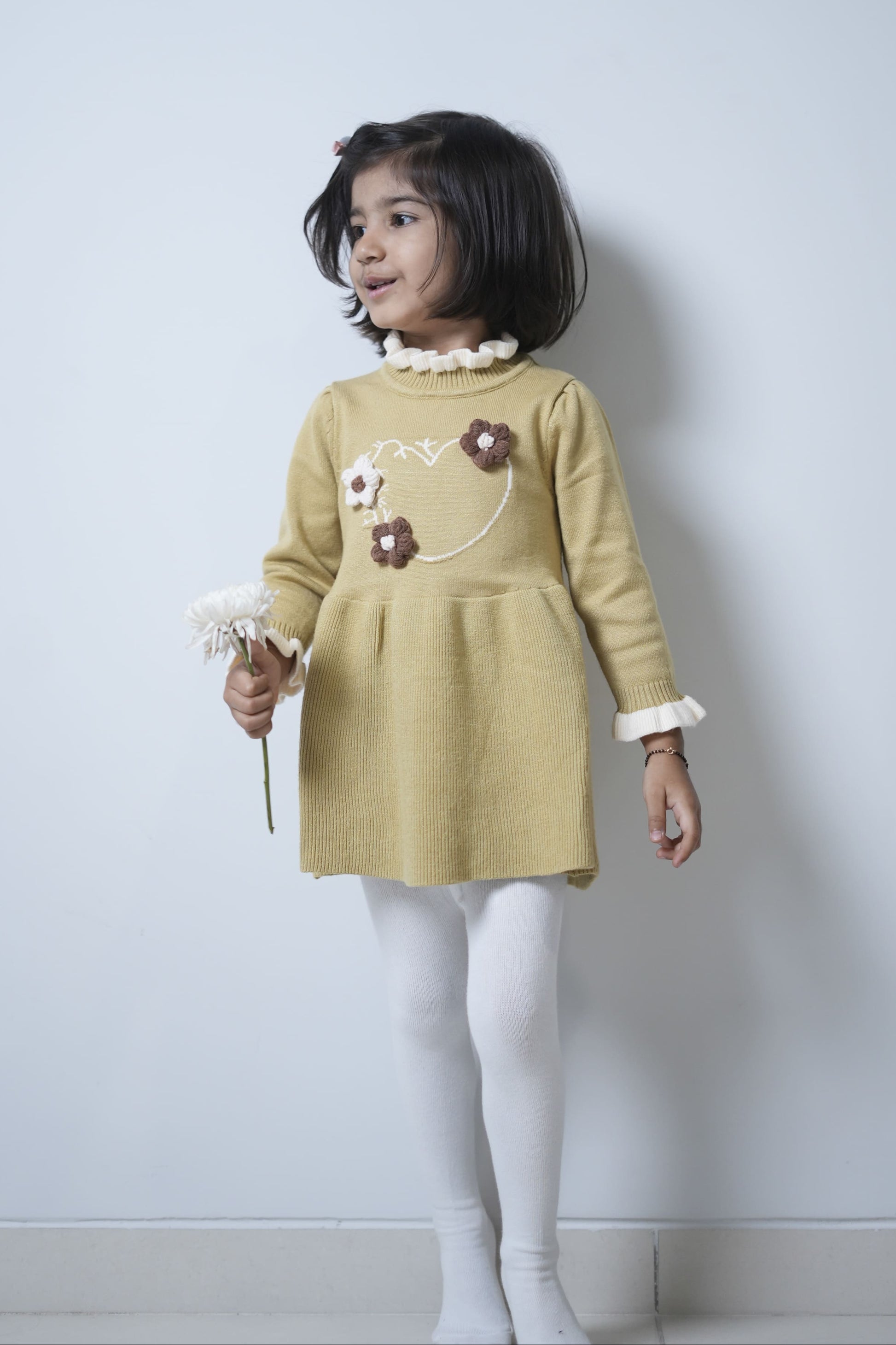 Young girl wearing a yellow dress with floral details against a plain background