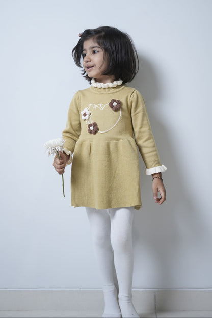 Young girl wearing a yellow dress with floral details against a plain background