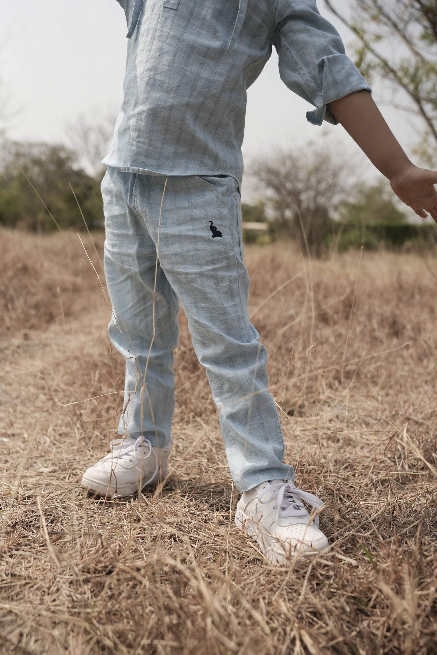 Person wearing light blue plaid shirt and pants with a black insect design, standing in a field.