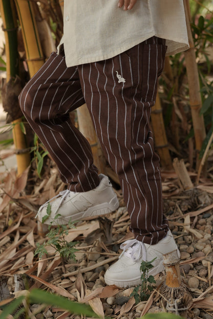 Person wearing brown striped pants and white shoes on a natural ground with plants.