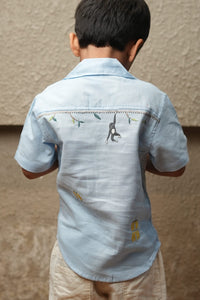 Light blue shirt with embroidery on a person against a beige wall