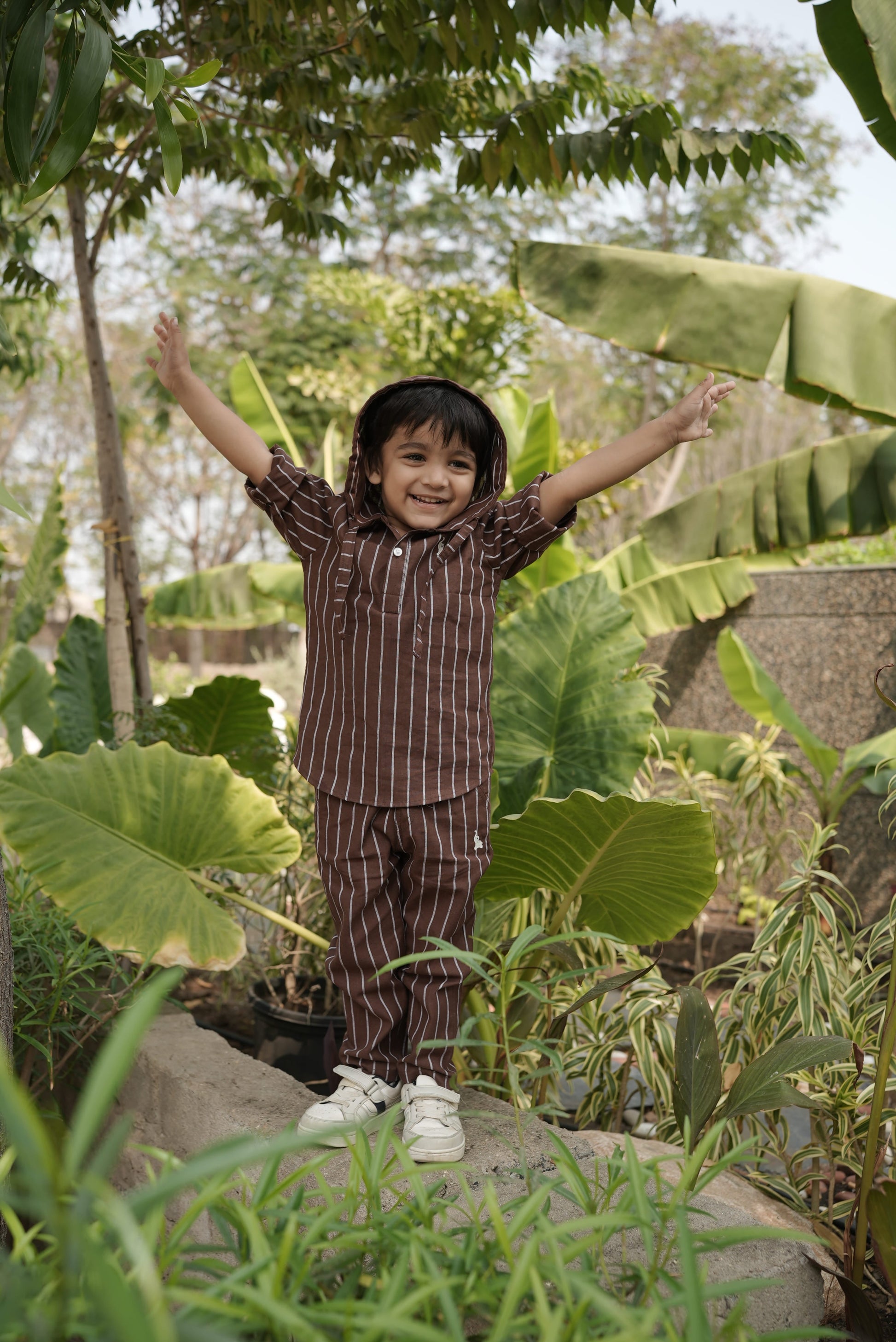 kid standing among large green leaves with a natural outdoor setting