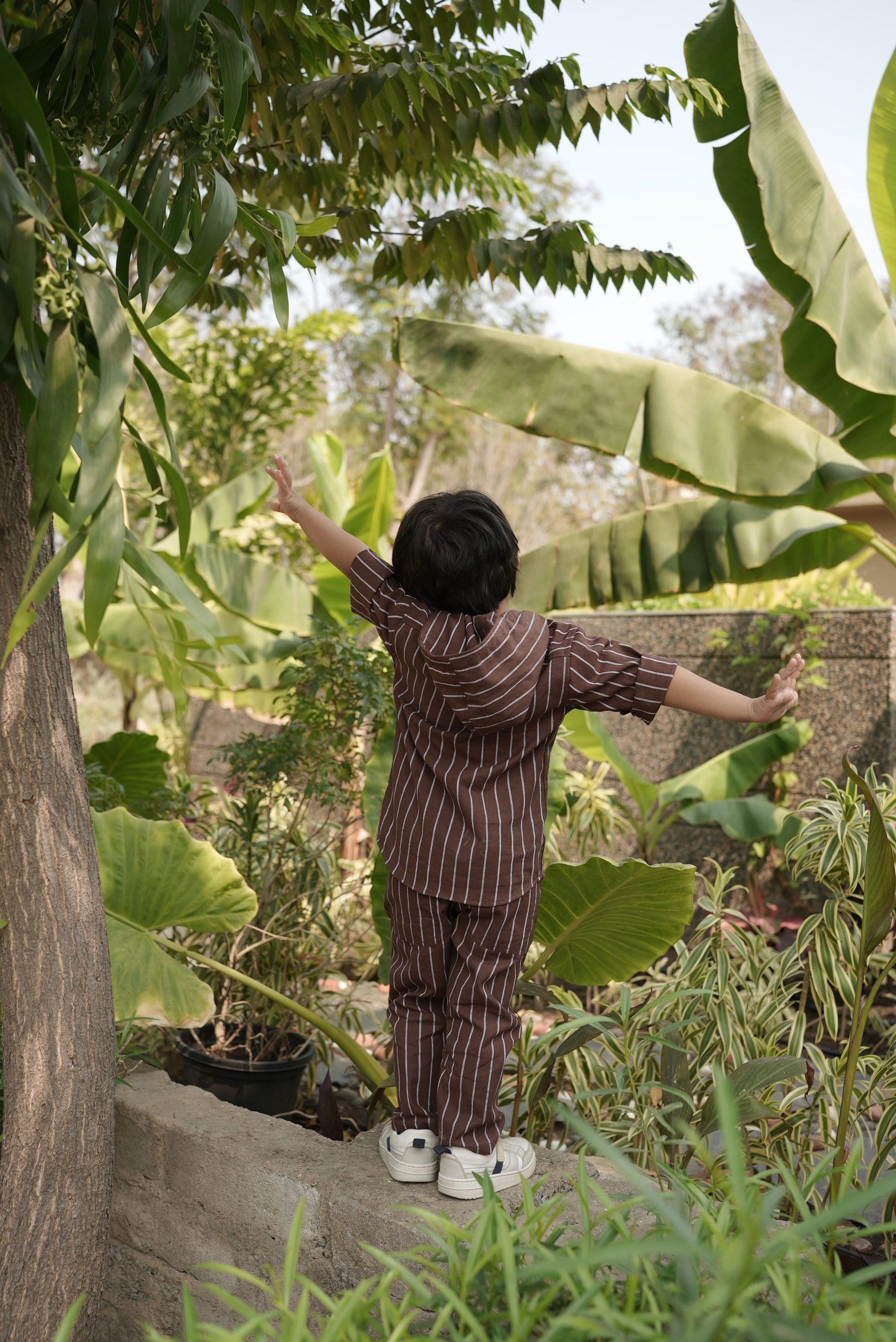 kid standing in a garden with large green leaves and plants