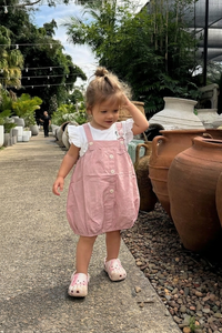 Child in a pink dress standing next to large pots in an outdoor setting