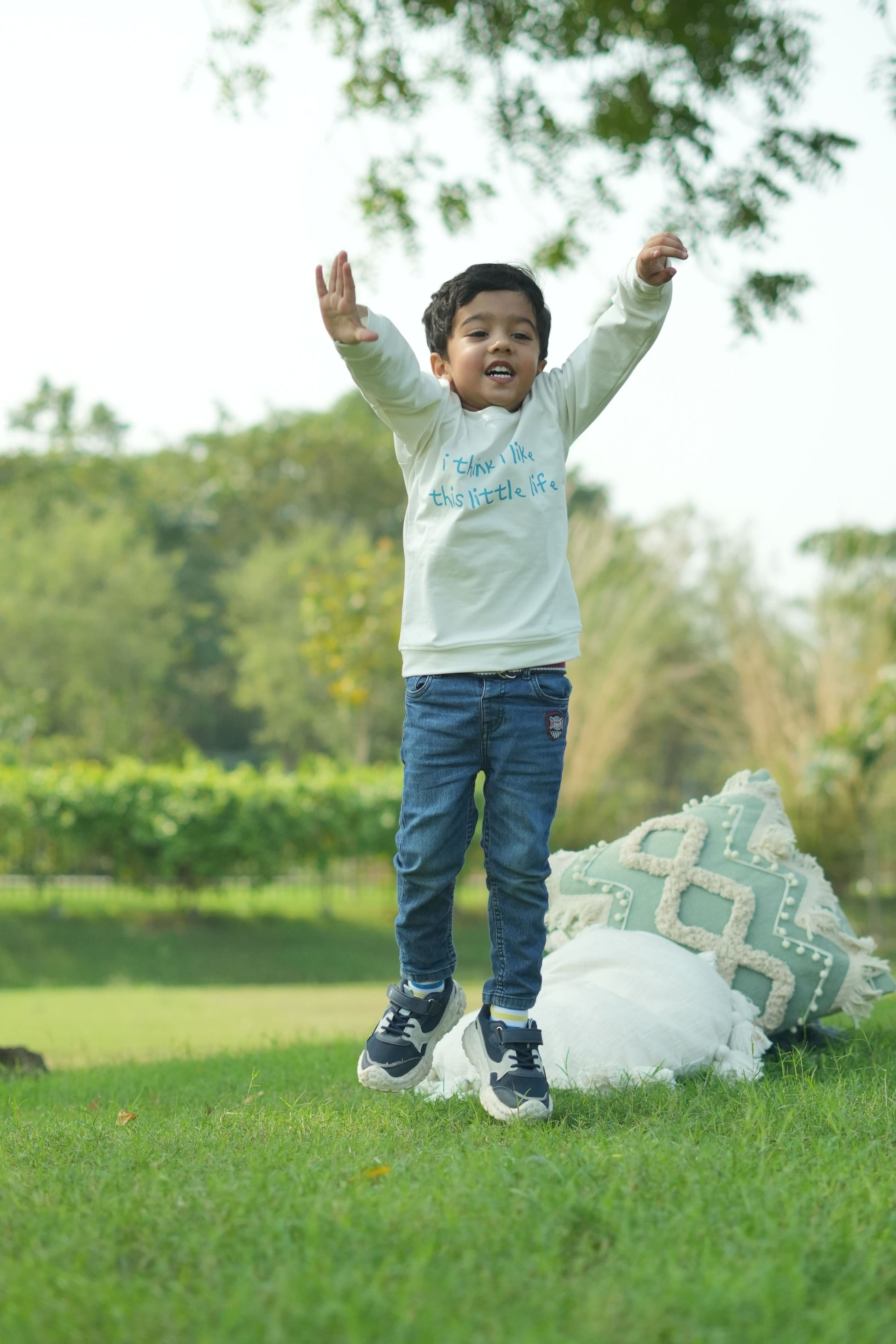 Child in a white shirt and blue jeans standing on a grassy area with trees in the background
