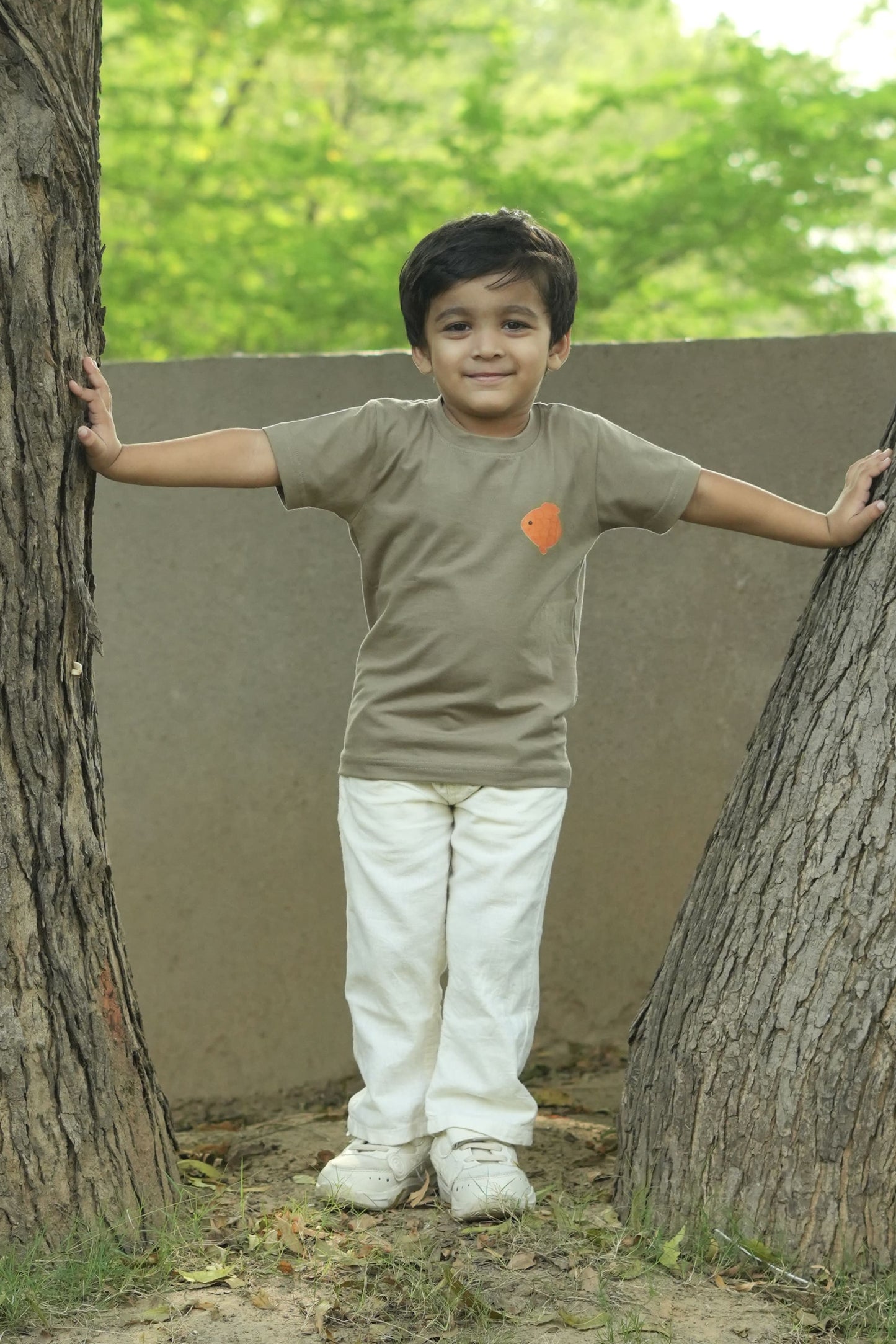 Child standing between two large trees with a neutral background
