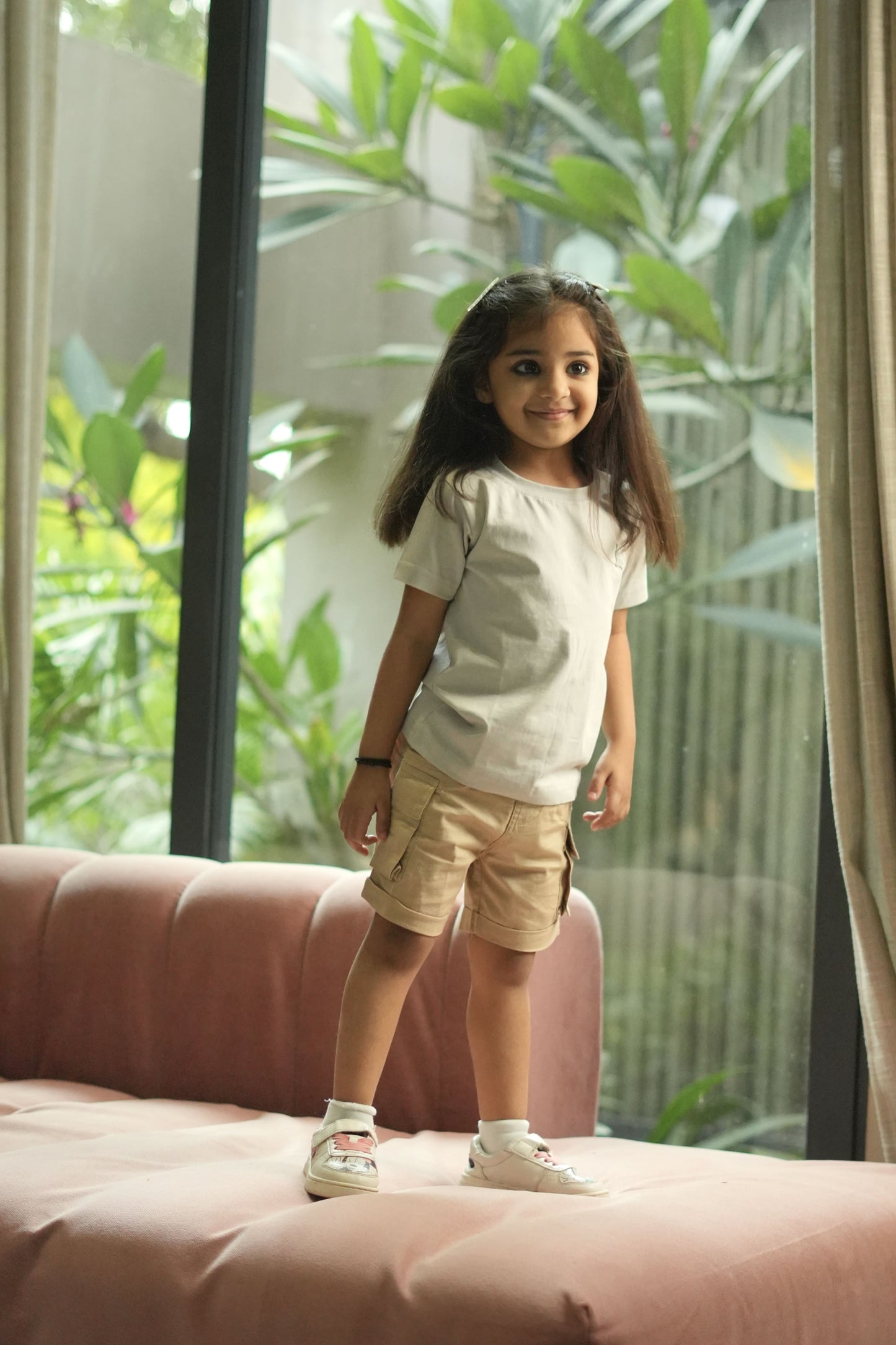Young girl standing on a pink couch with a blurred green outdoor background