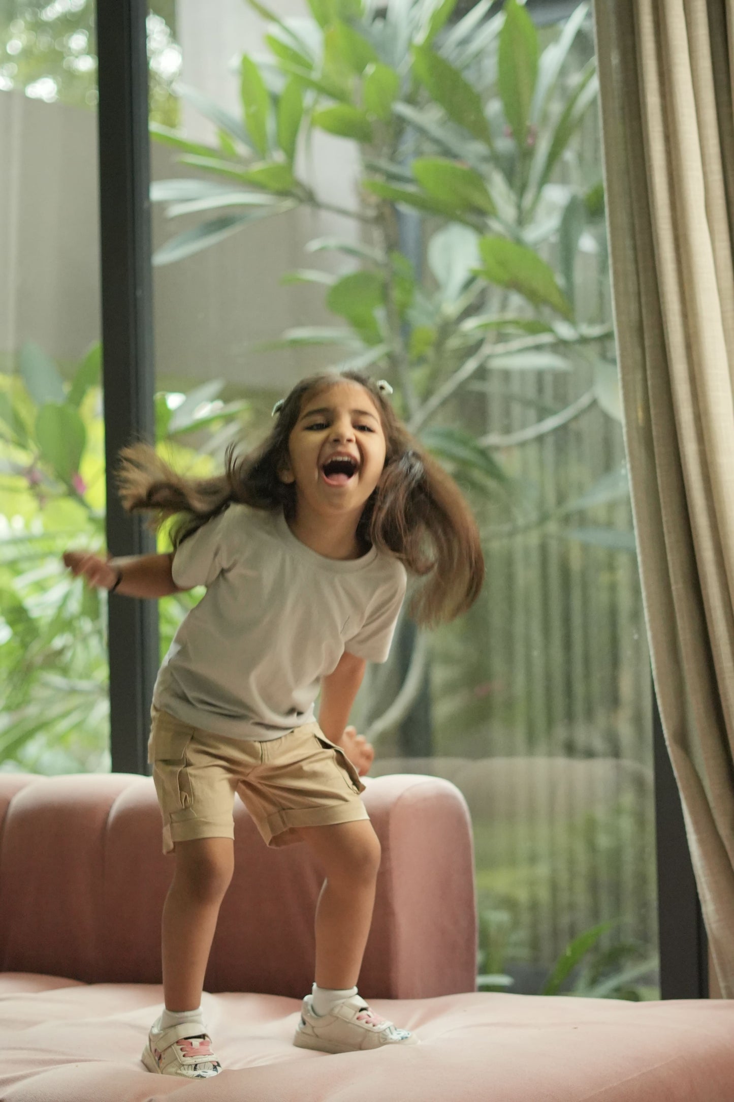 Child jumping on a bed with a view of greenery outside