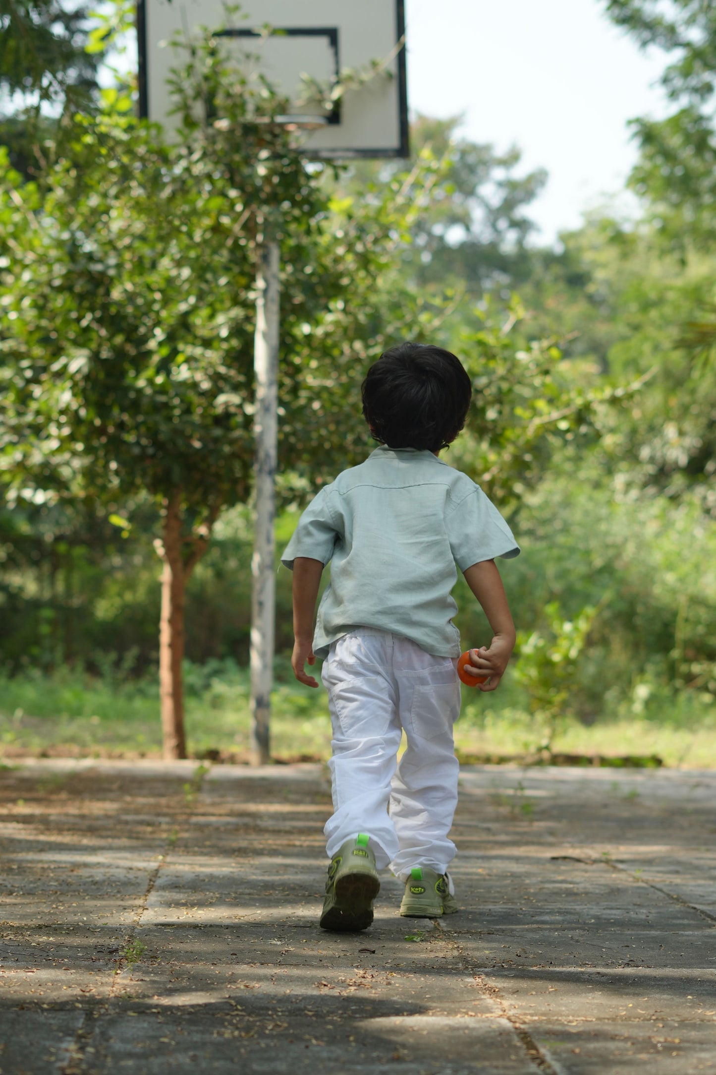 Child playing basketball on a court with trees in the background