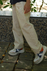 A toddler in beige natural linen pants reaching out to touch green leaves on a tree.